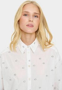Witte button-up shirt met zwarte wolk borduursels. Klassieke kraag en voorpand met knopen. Lichtgewicht, gladde stof.