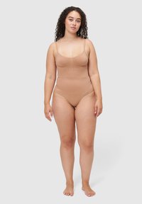 Naadloos beige bodypak met een gladde, rekbare stof, verstelbare spaghettibandjes en een aansluitend model. Heeft subtiele naaddetails en een beenuitsnijding.