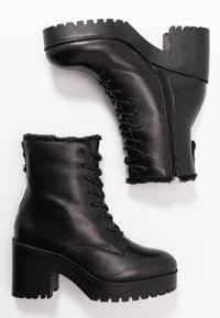 Zwarte leren enkellaarsjes met een dikke plateauzool, vetersluiting, zijrits en bontafwerking aan de bovenkant. Geheven profielzool.