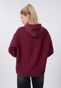 Sweat à capuche bordeaux avec un motif gaufré texturé ; coupe décontractée avec une poche kangourou et des manches à revers ; tissu doux.