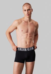 Schwarze Boxershorts mit einem weißen elastischen Bund, der das "CALVIN KLEIN"-Logo zeigt. Das Material wirkt glatt und enganliegend.