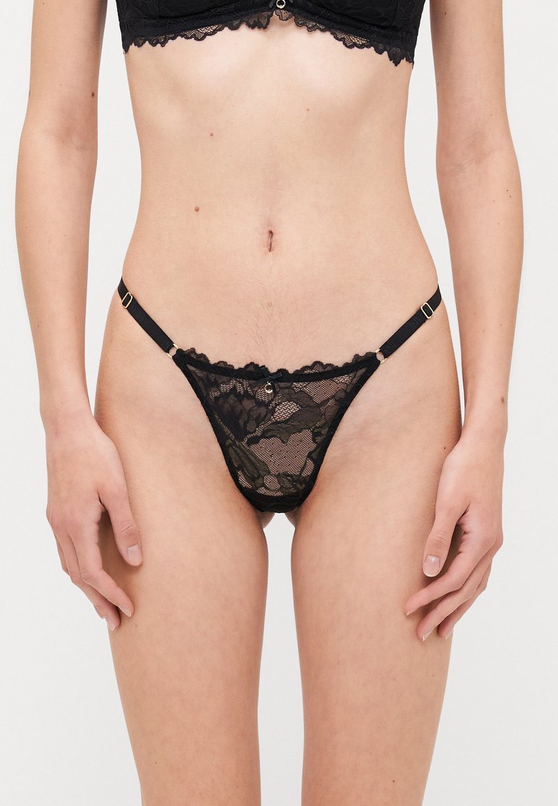 Black lace thong featuring intricate floral patterns, adjustable side straps, minimal coverage, and scalloped edges.