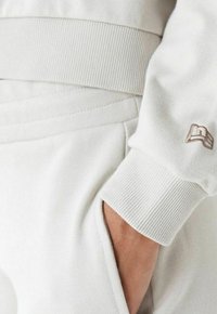 Sweatshirt grigio chiaro con polsini e vita a costine testurizzati, con un piccolo logo ricamato. Include un dettaglio di tasca laterale.