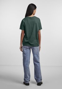 Camiseta de algodón de color verde oscuro con un corte relajado, mangas cortas y cuello redondo, combinada con vaqueros holgados de color azul claro y zapatos negros.