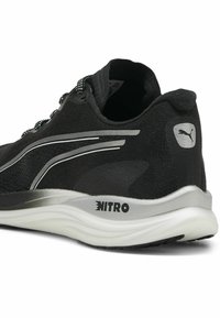 Fekete futócipő, textúrázott felső résszel, fényvisszaverő részletekkel és ezüst színű középtalppal, oldalán "NITRO" márkajelzéssel.