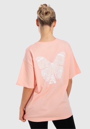 Helles rosa Baumwoll-T-Shirt mit kurzen Ärmeln, das auf der Rückseite einen großen weißen Schmetterlingsdruck zeigt, der fingerprint-ähnliche Muster präsentiert.