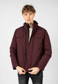 Giacca imbottita bordeaux con colletto alto, chiusura anteriore a pressione, due tasche sul petto e zip laterali. Texture liscia, design informale.