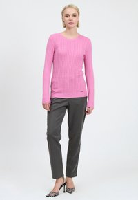 Suéter de punto rosa con patrón texturizado, cuello redondo y silueta ajustada, combinado con pantalones grises y zapatos de tacón alto con estampado.