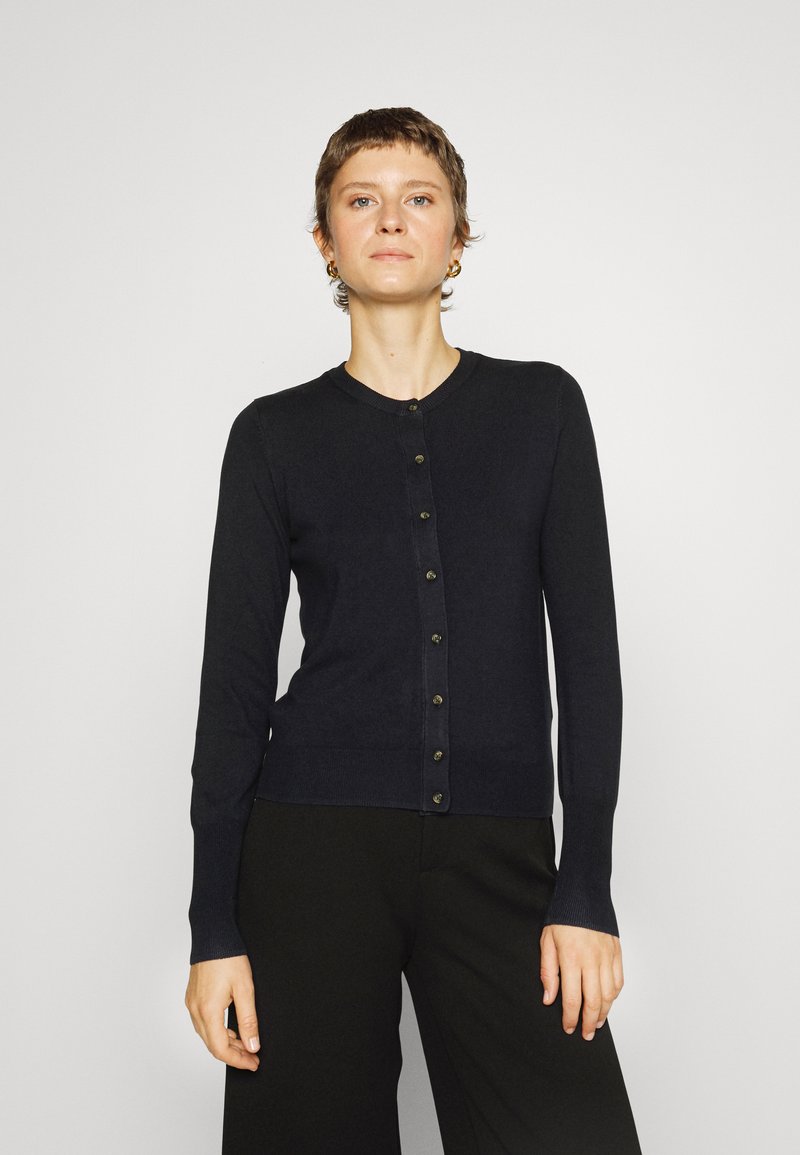 Gilet bleu marine avec un col rond, des manches longues et une rangée de boutons foncés sur le devant. Tissu tricoté lisse, design ajusté.