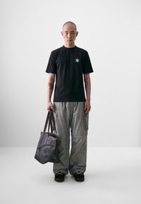 Black short-sleeve t-shirt with a small white symbol, gray cargo pants, and a gray tote bag with a long strap and decorative accents.