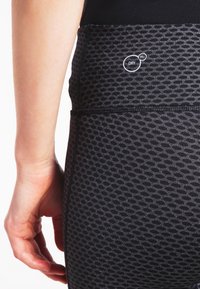 Czarne legginsy sportowe z fakturowanym, siateczkowym wzorem. Posiadają akcent logo "DRY CELL" na pasku w celu zarządzania wilgocią.