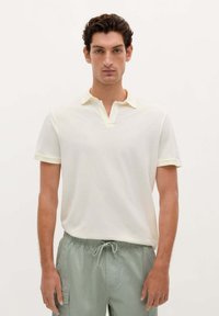 Polo-shirt van lichtgeel stof met korte mouwen, met een ondiepe kraag en subtiele textuur. Draag met lichtgroene shorts.