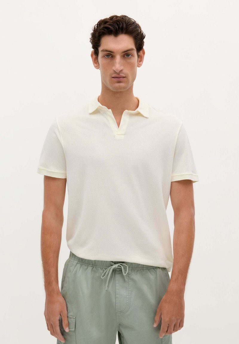 Polo-shirt van lichtgeel stof met korte mouwen, met een ondiepe kraag en subtiele textuur. Draag met lichtgroene shorts.