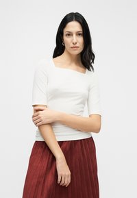 Λευκό εφαρμοστό τοπ με τετράγωνο ντεκολτέ και κοντά μανίκια, σε συνδυασμό με φούστα βυσσινί με πιέτες, παρουσιάζοντας ομαλές υφές και καθαρές γραμμές.