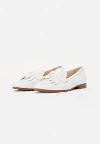 White leather loafers with fringed detailing at the front, smooth finish, low wooden heel, and rounded toe design.