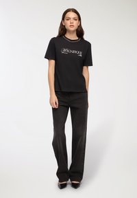 Czarna bawełniana koszulka z krótkim rękawem z białym napisem „MAGNIFIQUE”. Połączona z wysokim stanem ciemnych dżinsowych spodniami i czarnymi, eleganckimi szpilkami.