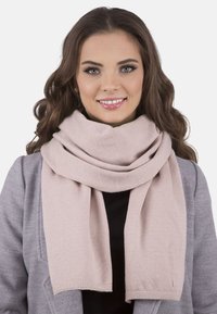 Světle růžový šátek vyrobený z měkké, teplé tkaniny, s hladkým povrchem a širokým, splývavým designem. Okraje jsou pečlivě dokončené.
