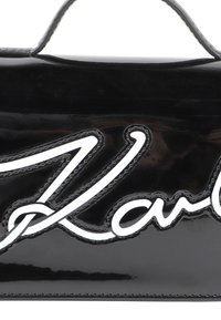 Sac à main noir en cuir verni avec un logo "Karl" blanc bien en vue, design épuré, texture lisse et courte poignée supérieure.