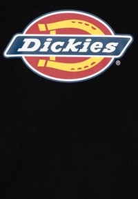 Juodas audinys t-shirt su dideliu, spalvingu apvaliu logotipu, kuriame yra raudonos, geltonos ir mėlynos spalvos elementai, aiškiai matomas žodis "Dickies".
