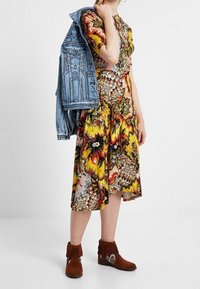 Blommönstrad knälång klänning i livliga gula, röda och gröna färger; kombinerad med en denimjacka och bruna mocka ankelstövlar.