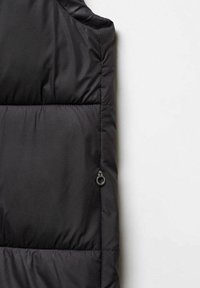 Veste sans manches noire matelassée, présentant une texture lisse et brillante, avec des segments horizontaux cousus et une poche zippée sur le côté.