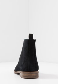 Černé semišové Chelsea boty s elastickými bočními panely a nízkým hromadným podpatkem, se strukturovaným povrchem a kontrastní hnědou podrážkou.