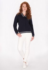 Giacca in maglia navy con colletto e polsini a righe bianche, abbinata a pantaloni bianchi aderenti e sneaker bianche. Texture liscia, design casual.