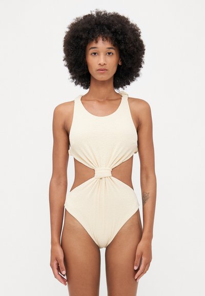 Cream-colored one-piece swimsuit with textured fabric, round neckline, cut-outs at the sides, and knot detail at the waist.