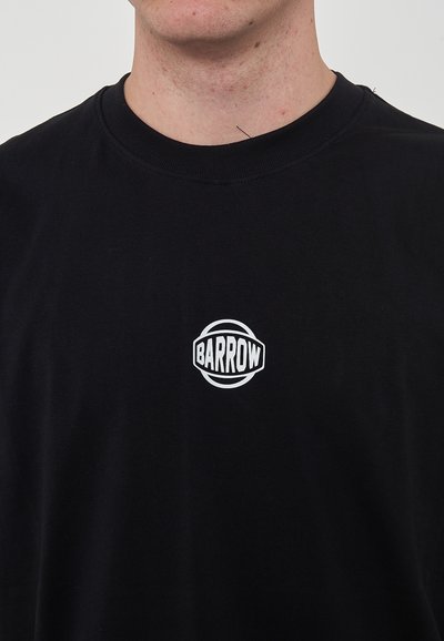 Camiseta de algodón negra con un logo blanco redondo que presenta el texto "BARROW" en el lado izquierdo del pecho, diseño sencillo de cuello redondo.