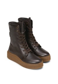 Bottes en cuir marron avec un bout arrondi, une tige haute et une semelle en caoutchouc présentant un motif rainuré texturé. Lacets et œillets sur le devant.