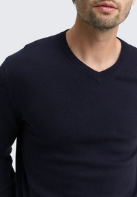 Marineblauer V-Ausschnitt-Pullover aus weichem Strickmaterial, mit gerippten Bündchen und Saum, glatter Textur und taillierter Silhouette.