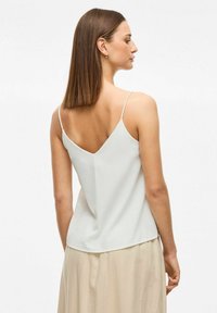 Camisola gri deschis cu bretele subțiri, spate în formă de V, realizată dintr-un material neted, având un croi lejer și un design minimalist.
