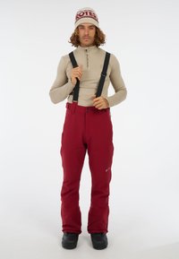Rode sneeuwbroek met verstelbare zwarte banden, gecombineerd met een beige longsleeve en zwarte laarzen, met een snug fit voor winteractiviteiten.