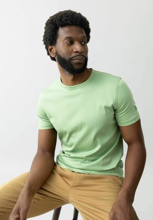 Mintgrünes Kurzarm-T-Shirt mit Rundhalsausschnitt und dezenten Ärmeldetails, kombiniert mit hellbeigen Hosen. Glatte Stofftextur.