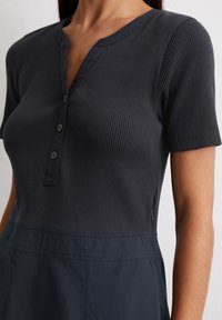 Close-up of a person wearing a dark ribbed shirt with a buttoned placket. The fabric has a textured appearance against a plain background.