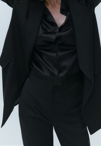 Black oversized blazer over a black satin button-up shirt, paired with tailored black trousers, creating a sleek, monochromatic look.