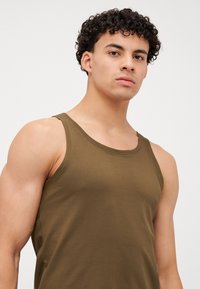 Débardeur vert olive en coton doux avec un col rond et de larges bretelles, présentant une texture lisse et des détails de couture minimalistes.