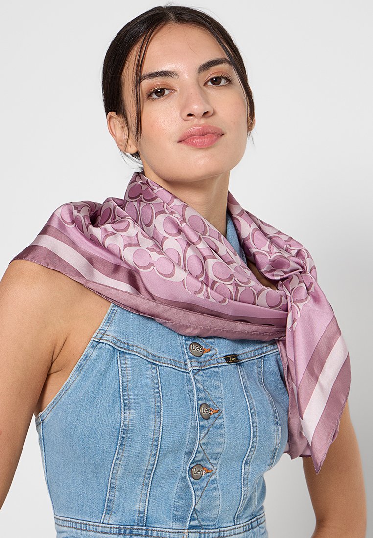 Écharpe en soie de couleur rose clair avec des motifs circulaires et des bords rayés. L'écharpe est drapée autour du cou, mettant en valeur une texture lisse.