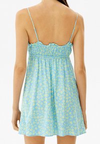 Blå blommig klänning med justerbara spaghettiband, samlad byst och utställd kjol. Har gula blommor på en ljusblå bakgrund.