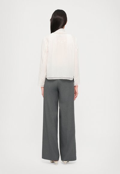 Blusa ligera y transparente con borde de encaje y pliegues verticales, combinada con pantalones de pierna ancha grises de alta cintura. Textura suave, colores neutros.