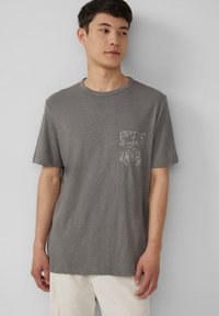 Grijze t-shirt met korte mouwen, gemaakt van zacht stof, met een borstzakje met een subtiele botanische print. Ontspannen pasvorm en ronde hals.