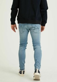 Vaqueros de un azul claro con un corte ajustado, que presentan bolsillos traseros prominentes con costuras en forma de diamante y una textura deslavada. Combinados con calzado oscuro.