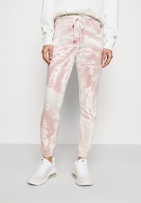 Lekko różowe i białe spodnie dresowe w stylu tie-dye z elastycznym pasem i regulowanym sznurkiem, zestawione z białymi butami sportowymi.