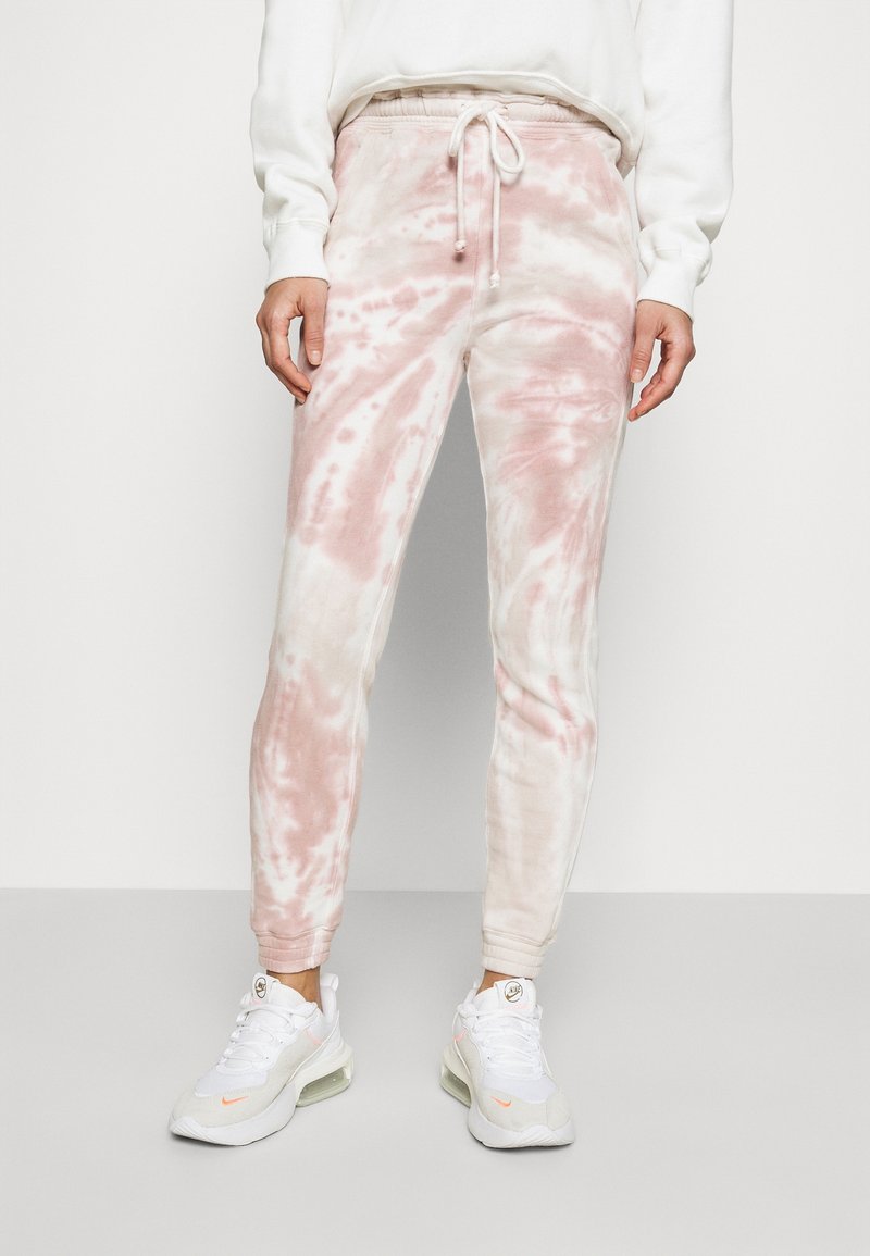 Lekko różowe i białe spodnie dresowe w stylu tie-dye z elastycznym pasem i regulowanym sznurkiem, zestawione z białymi butami sportowymi.