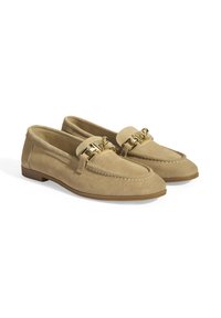 Beige suède loafers met een ronde neus, klassieke stiksels en een gouden hardware-detail op de band. Vlakke zool met minimale textuur.
