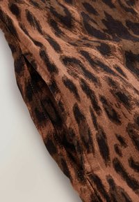 Tissu marron avec motif léopard noir, légèrement froissé, avec un ourlet cousu le long d'un bord.