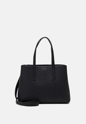 Czarna torba typu tote Calvin Klein z podwójnymi uchwytami i odpinanym paskiem na ramię, z subtelnym tłoczonym wzorem logo i srebrną tabliczką z nazwą marki.