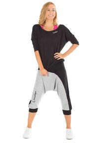 Pantalones harem en negro y gris con un corte holgado, que presentan una parte superior negra ancha y costuras deportivas, combinados con zapatillas blancas y un acento de logo.