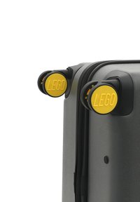 Gray suitcase with yellow LEGO-branded wheels and black accents. Features a textured surface and a zipper closure.