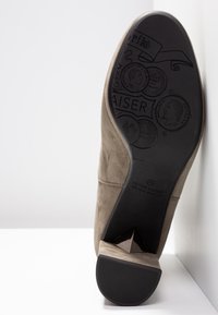 Semelle d'une chaussure en daim taupe montrant une semelle en caoutchouc noir avec des motifs de pièces embossés et le logo Peter Kaiser.